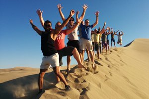 Group of people enjoying and posing with raised arms on a sand dune.